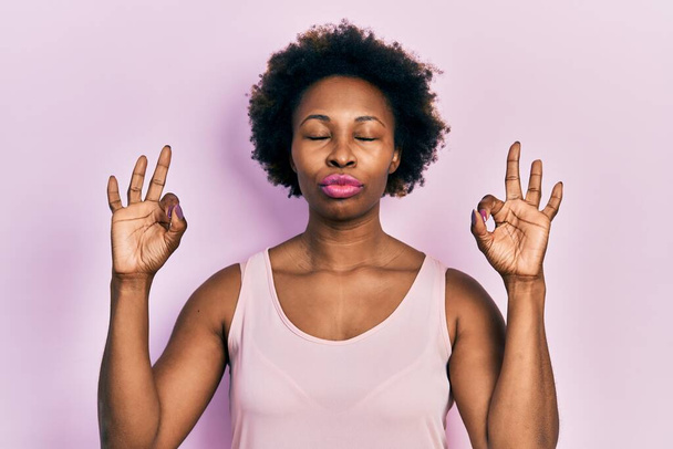 Jovem afro-americana vestindo camiseta casual sem mangas relaxar e sorrir com os olhos fechados fazendo gesto de meditação com os dedos. conceito de ioga.  - Foto, Imagem