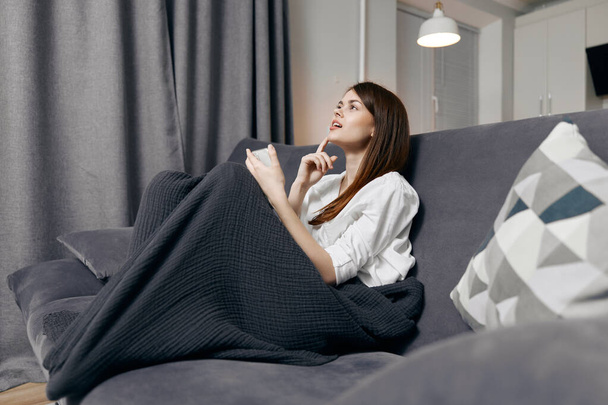 жінка сидить на дивані під ковдрою і мобільний телефон в руці
 - Фото, зображення