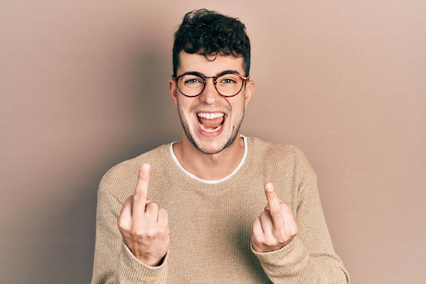 junger hispanischer Mann in lässiger Kleidung und Brille, der den Mittelfinger zeigt, wie er dich fickt, mit schlechter Miene, Provokation und unhöflicher Haltung. Kreischen erregt  - Foto, Bild