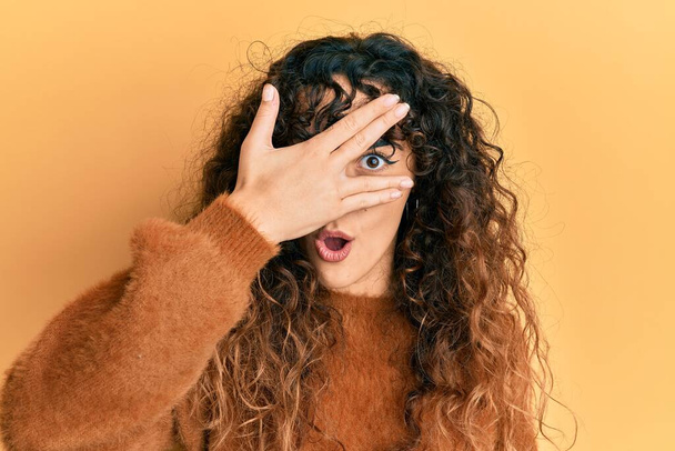 Menina hispânica jovem vestindo roupas casuais espreitando em choque cobrindo rosto e olhos com a mão, olhando através dos dedos com medo  - Foto, Imagem