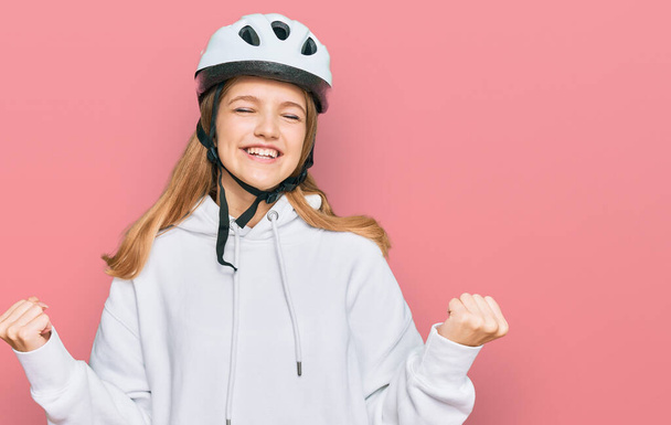 Beautiful young caucasian girl wearing bike helmet very happy and excited doing winner gesture with arms raised, smiling and screaming for success. celebration concept.  - Photo, Image