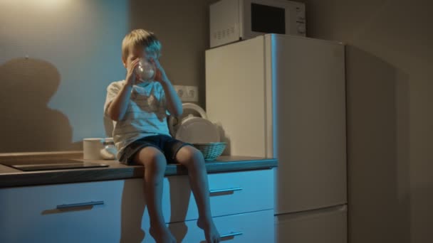 Kleiner Junge sitzt auf Küchentisch und trinkt nachts Milch - Filmmaterial, Video