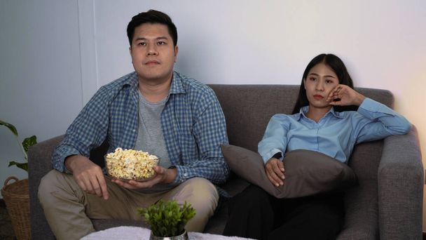 Šťastný mladý asijský pár položit pohovku v jejich útulný obývací pokoj sledování filmu v televizi a jíst popcorn společně ve večerních hodinách doma - Fotografie, Obrázek