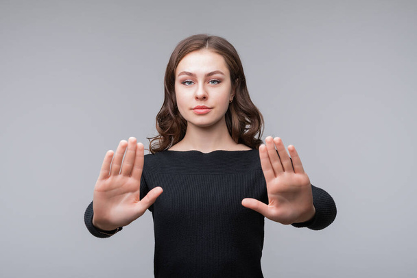 Портрет серьезной девушки, стоящей с протянутыми руками, показывающей стоп-жест, отказывающейся от предложения, изолированной на сером фоне - Фото, изображение