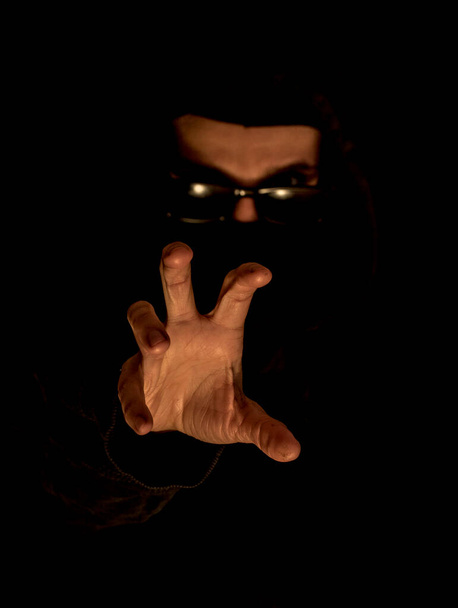 homem mascarado de roupas pretas usando óculos escuros, mão estendida para roubar algo, criminalidade - Foto, Imagem