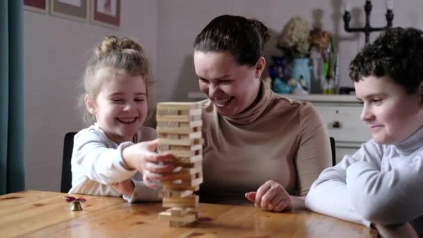 Gelukkig jong volwassen moeder spelen met twee leuke kinderen. Een speelse moeder helpt kleuters met het bouwen van een toren van houten blokken in de woonkamer. Educatieve spelletjes met het hele gezin. - Video