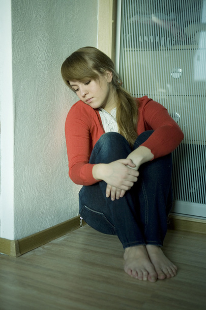 Młoda smutna dziewczyna siedzi w rogu pokoju. Problemy nastolatków - Zdjęcie, obraz