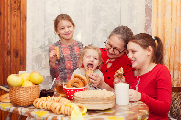 Donna russa con tre nipoti a tavola con pancake, panna acida e marmellata bere tè - Foto, immagini
