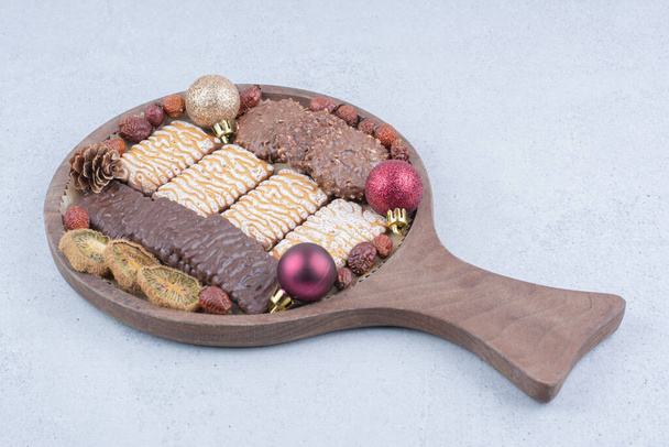 Διάφορα μπισκότα, αποξηραμένα φρούτα και μπάλες Χριστουγέννων σε ξύλινη σανίδα. Υψηλής ποιότητας φωτογραφία - Φωτογραφία, εικόνα