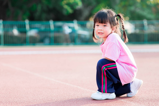 3-4-летняя азиатка притворяется бегущей на беговой дорожке. Милые дети занимаются спортом на открытом воздухе летом. Счастливый ребенок носил розовую рубашку. - Фото, изображение