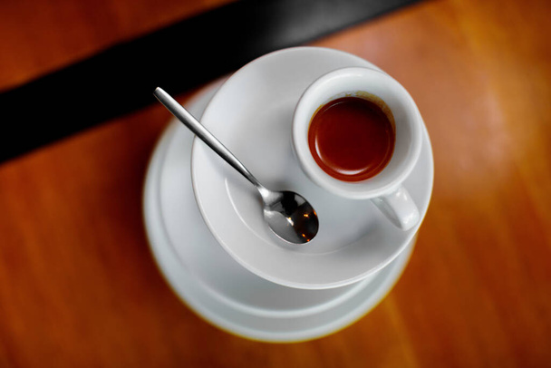 Tabağında kaşık olan beyaz bir fincan espresso, ahşap masada duruyor. - Fotoğraf, Görsel