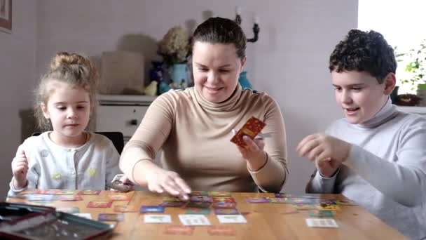 Επιτραπέζια εκπαιδευτικά παιχνίδια με όλη την οικογένεια σπίτι. Χαρούμενη Καυκάσια νεαρή μητέρα του αγοριού και της κοπέλας παίζουν το τραπέζι του παιχνιδιού. Δημιουργική ανάπτυξη παιδιών προσχολικής ηλικίας. Κοινά παιχνίδια γονέων και παιδιών - Πλάνα, βίντεο