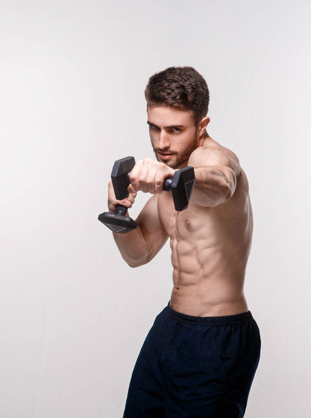 Young athlete on a white background lifts dumbbells. training a bearded man athletic build - Fotografie, Obrázek