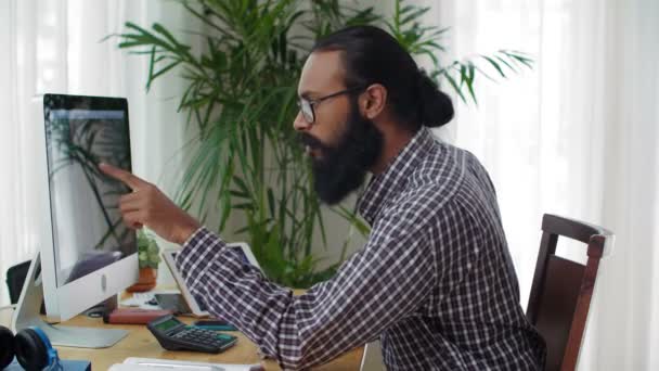 Bloqueio do jovem indiano com barba sentada na mesa, olhando para a tela do computador, apontando com o dedo em algum lugar do código, e depois começando a digitar novo código de software - Filmagem, Vídeo