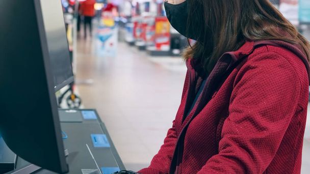 Mädchen mit Maske und Handschuhen gegen Virus kauft konkaven Monitor im Geschäft - Foto, Bild