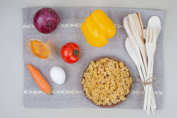 Сирі макарони з овочами на дерев'яній тарілці на скатертині
 - Фото, зображення
