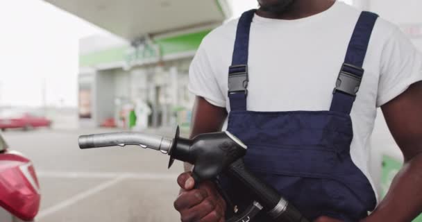 Schwarzafrikanischer Tankstellenangestellter mit Pistole zum Betanken eines Autos. Ein Tankstellenangestellter steckt eine Waffe zum Betanken in ein Fahrzeug und wartet auf das Betanken des Tanks. Porträt eines schwarzen Arbeiters - Filmmaterial, Video
