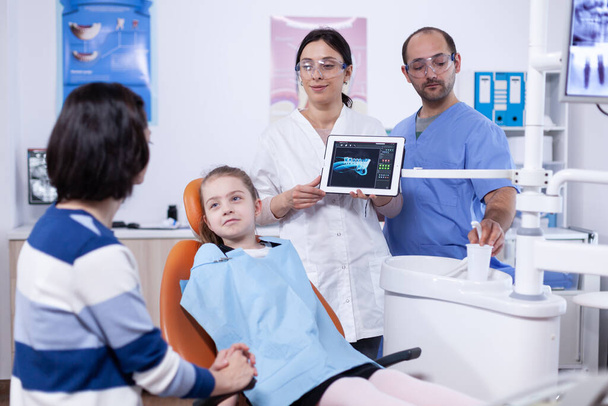 Οδοντίατρος και ασθενής σχολιάζοντας κοιλότητα θεραπεία στην εφαρμογή δισκίων - Φωτογραφία, εικόνα