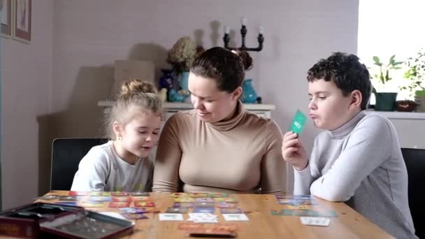 Happy mam is het spelen van een board-based educatieve creatieve dobbelstenen kaartspel met de kinderen in de lichte woonkamer aan de tafel. - Video