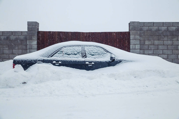 car parked near the fence is completely covered with snow - Foto, imagen