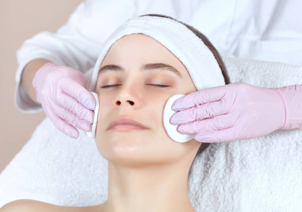 Il medico cosmetologo purifica con un tonico la pelle del viso di una bella, giovane donna in un salone di bellezza.. - Foto, immagini