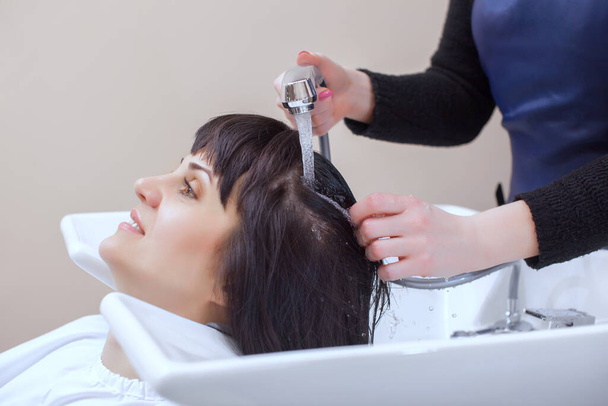Il parrucchiere lava i capelli del cliente con lo shampoo in un salone di bellezza. - Foto, immagini