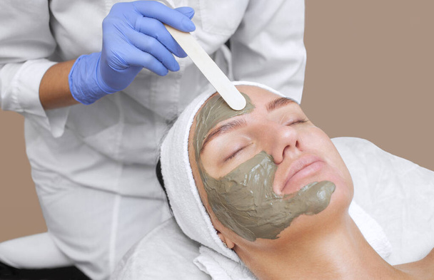 El procedimiento para aplicar una máscara de arcilla a la cara de una mujer hermosa. Tratamientos de spa y cuidado de los gatos en el salón de belleza. - Foto, imagen