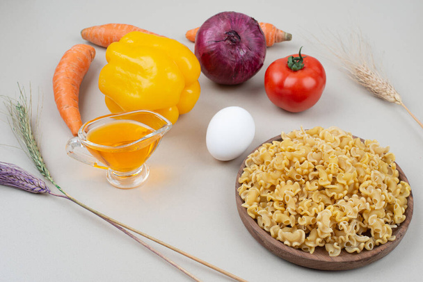 Raw macaroni with vegetables on wooden plate - Photo, Image