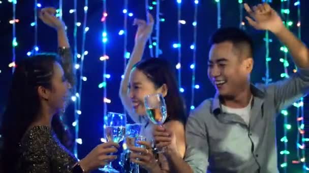 3人の恍惚とした若いアジアの人々の中のショットシャンパンのグラスを保持し、ナイトクラブでリズミカルな音楽に陽気に踊る - 映像、動画