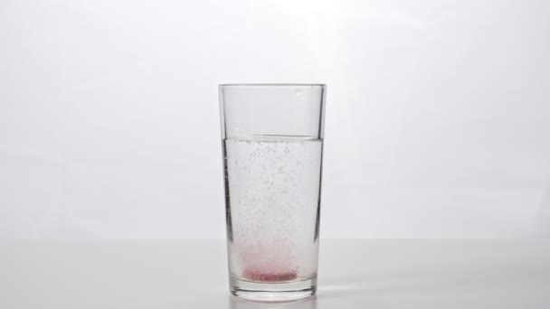 Tabletka musująca wpada do szklanki wody na białym tle - Materiał filmowy, wideo