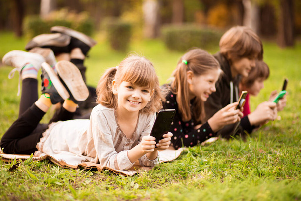 Retrato al aire libre de niña con amigos jugando con teléfonos al aire libre  - Foto, imagen