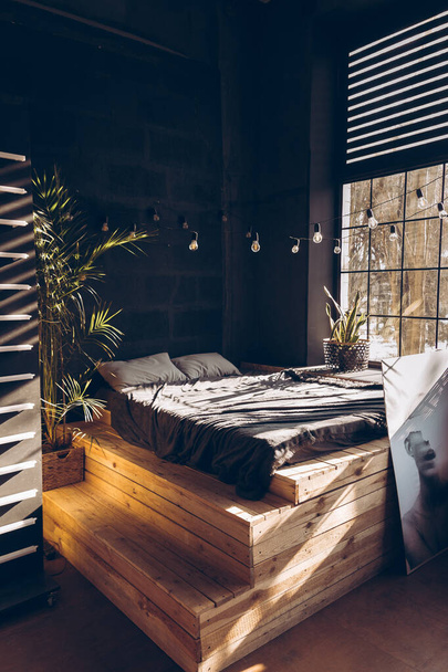 ダーク家具付きのモダンな部屋のインテリア。ロフトスタイルの寝室。黒いベッド付きの木製の階段付きのベッド - 写真・画像