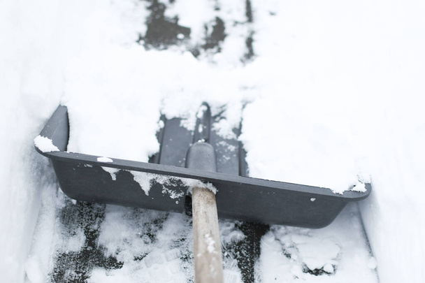 Концепция очистки снега. Черная лопата в снегу. Лопата для уборки снега в снежном заносе на фоне дорожки, инструмент для уборки снега - Фото, изображение