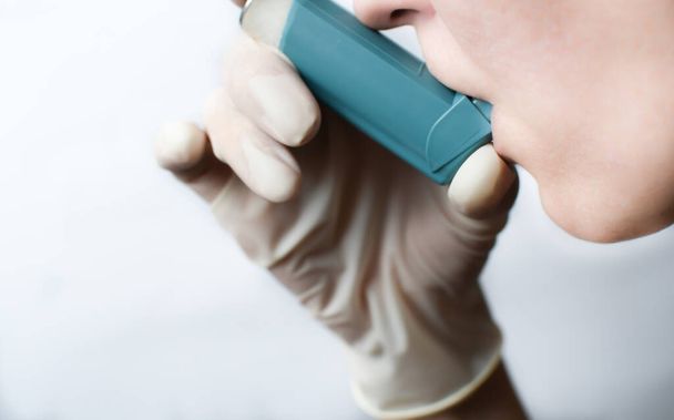Μια γυναίκα χρησιμοποιεί έναν εισπνευστήρα κατά τη διάρκεια μιας κρίσης άσθματος. Χρήση εισπνεόμενου μπλε άσθματος για την ανακούφιση από μια κρίση άσθματος - Φωτογραφία, εικόνα