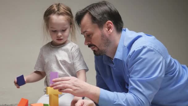 Father and daughter play colorful cubes in the childrens room on floor. Dad and daughter are building family home. Teaching child through play activities. Happy family. Educational games for children - Footage, Video