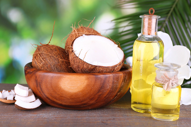 Coconuts and coconut oil on wooden table, on nature background - Photo, Image