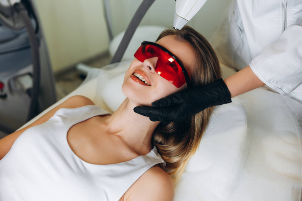 Cosmetologist doing laser epilation to her client. Adult woman lying on medical table in beauty clinic, having laser hair removal in professional beauty salon. - Photo, Image