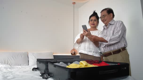 Mediana toma de pareja de ancianos de pie en la maleta abierta en la habitación del hotel y haciendo selfie en la cámara del teléfono - Metraje, vídeo