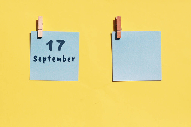 17. September. 17. Tag des Monats, Kalenderdatum. Zwei blaue Blätter zum Schreiben auf gelbem Hintergrund. Draufsicht, Kopierraum. Herbstmonat, Tag des Jahres. - Foto, Bild
