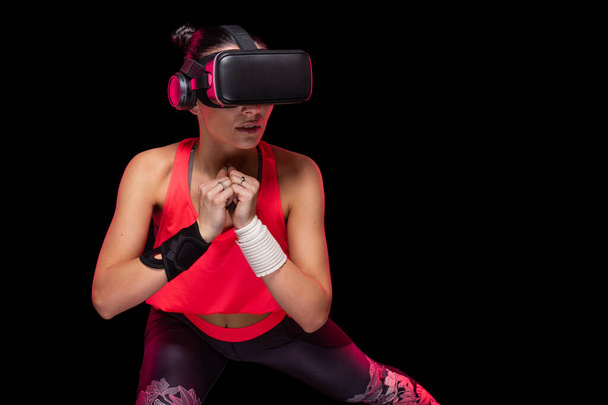 Gyönyörű sportos kaukázusi sportoló nő edzés rózsaszín alsónemű fekete háttér - Stúdió forgatás során torna edzés gyakorlása visel hi tech futurisztikus vr szemüveg - Fotó, kép