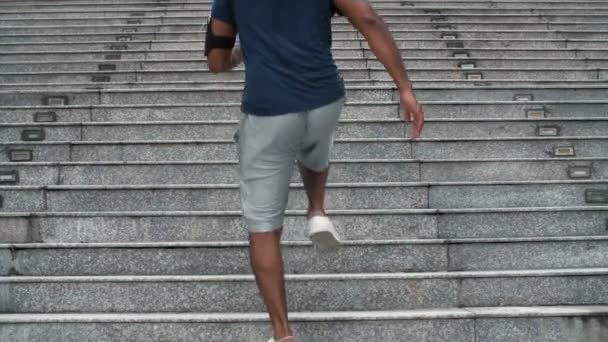 Вид сзади на человека с темной кожей в спортивной одежде, бегущего наверх в городской зоне - Кадры, видео
