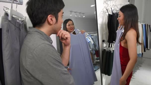 Średnie ujęcie azjatyckiej pary wybierającej sukienkę w sklepie - Materiał filmowy, wideo