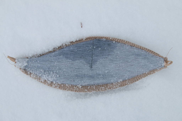 Közelkép a fa arc maszk feküdt a friss hó során használt covid-19 vírus zárlat, mint a védelem a napi séta madár szeme a fehér háttér - Fotó, kép