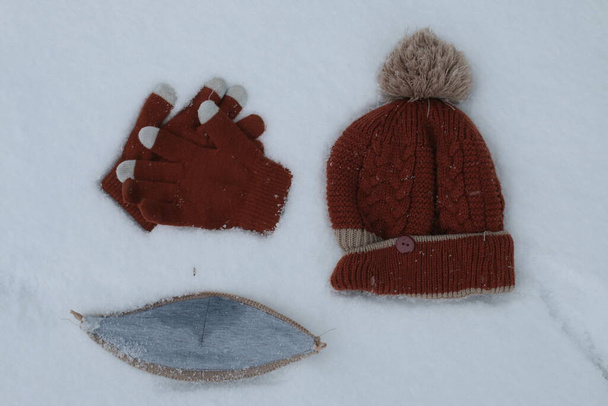 Blisko do maski wełnianej rękawiczki bobble kapelusz wełniany czekolada kolor zestaw położony w swieżych opadach śniegu biały śniegu w wyraźnym kontraście do brązowej wełny odzieży w zimowym widokiem na oko ptaka - Zdjęcie, obraz