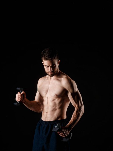 A man on a black background with dumbbells in his hands. young bearded athlete. - Photo, Image