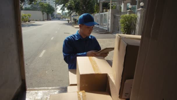 Colpo medio di giovane asiatico in uniforme blu tenendo tablet in mano, strisciando web-papers, alla ricerca di informazioni riguardanti pacchi - Filmati, video