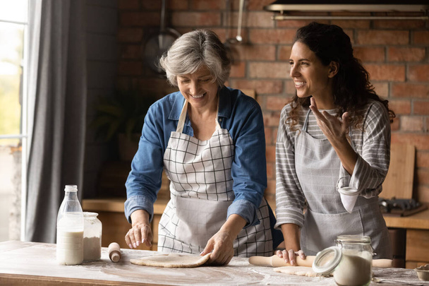 Happy adult daughter with senior mom bake at home kitchen - Foto, Bild
