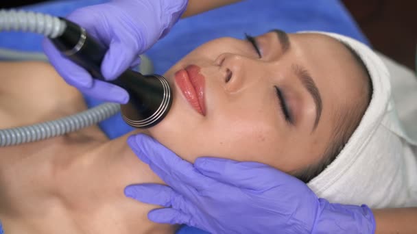 Kapalı gözlü Asyalı kadının tedavi masasına uzanması ve yüz kaslarının özel ekipmanlarla uyarılması. - Video, Çekim
