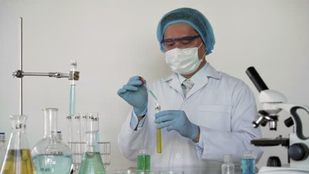Onherkenbare mannelijke laboratoriummedewerker in beschermende kleding en brillen die vloeistof in de kolf doet terwijl hij medisch onderzoek doet - Video