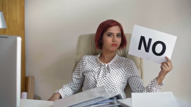 Opsluiting van de jonge Indiase zakenvrouw zittend op een stoel in haar kantoor met naamplaatje in haar hand, kijkend naar de camera en nee zeggend om aan te bieden - Video